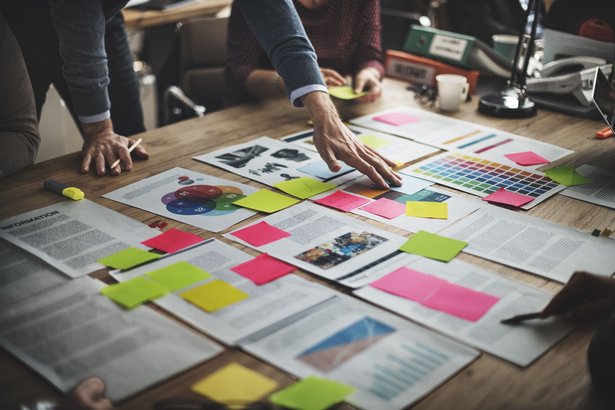 A-person-reaching-for-a-paper-on-a-table-full-of-paper-and-sticky-notes